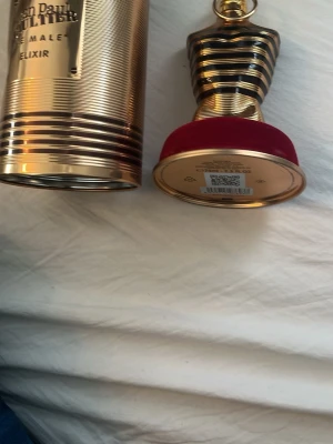 Jean Paul Gaultier Le Male Elixir - Lyxig parfym i en ikonisk guldfärgad flaska formad som en manlig torso med röda detaljer. Kommer i en elegant guldfärgad metalltub. Doften är djup och intensiv, perfekt för dig som vill sticka ut.