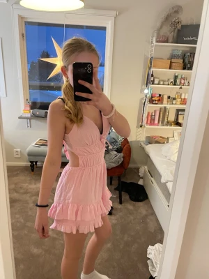 Söt rosa kortklänning med volanger - Superfin ljusrosa kortklänning med volanger. Klänningen har ett knyte på baksidan. Klänningen är helt ny då jag inte ens tagit bort lappen. Man kan justera banden på klänningen och den har även shorts under. Säljer den då den inte kommer till användning. Orginalpris 239 kr 💕💕