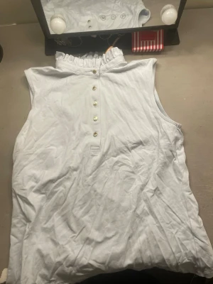 Vit ärmlös topp Holly & Whyte - Snygg vit ärmlös topp från Holly & Whyte by Lindex med volangkrage och knappar framtill. Tillverkad i mjuk bomull, perfekt för en fräsch och stilren look. Passar till både jeans och kjol.