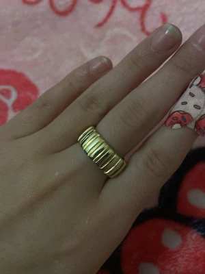 Bred guldfärgad ring med räfflor - Säljer en bred guldfärgad ring med räfflad design runt hela ringen. Ringen har en chunky känsla och ger ett statement till din stil. Perfekt för dig som gillar att sticka ut med accessoarer. Materialet ser ut som metall med blank finish. Storlek ungefär 7