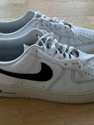 Nike Air Force 1 vita sneakers - Klassiska Nike Air Force 1 sneakers i vitt läder med svart swoosh på sidan. I väldigt bra skick. Innersulor medföljer också.