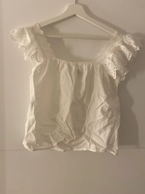 Vit blus med spetsdetaljer Zara - Söt vit blus från Zara med breda axelband och volangprydda spetsdetaljer. Toppen har en rak passform. Säljs inte längre, men aldrig använt. Pris kan diskuteras.