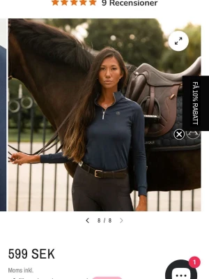 Marinblå långärmad ridtopp från Ariat - Snygg marinblå långärmad ridtopp från Ariat med half zip-dragkedja framtill. Tillverkad i ett stretchigt syntetmaterial som andas, perfekt för ridning. Diskret logga på bröstet och figurnära passform.