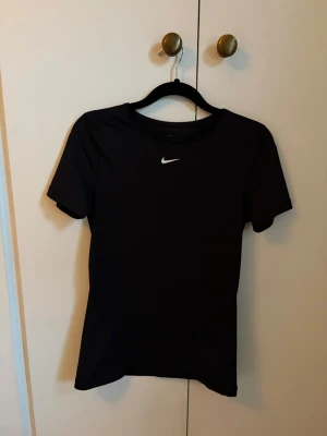 Svart Nike sport t-shirt - En svart sport t-shirt från Nike med klassisk vit logga på bröstet. T-shirten har rund halsringning och korta ärmar. Tillverkad i ett lätt och funktionellt material som passar perfekt till träning och aktivitet.