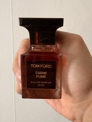 Tom Ford Ébène Fumé EdP 30 ml - Tom Ford Ébène Fumé Eau de Parfum i en elegant, fyrkantig glasflaska med mörkbrunt lock och guldtext. Flaskan rymmer 30 ml och har en lyxig, stilren design som känns exklusiv och modern. Nypris mellan 1300-1800 kr. 29/30 ml kvar på flaskan. 