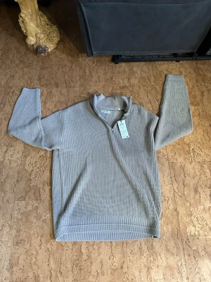 Beige halvzip tröja från Jack & Jones - Snygg beige stickad tröja från Jack & Jones med halvzip och hög krage. Tröjan har ett diskret rutmönster i stickningen och ribbade muddar vid ärmslut och nederkant. Perfekt för en avslappnad men stilren look. Ny pris 599  (bara testad)