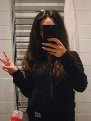 Svart zip hoodie med huva - Säljer en svart hoodie med dragkedja och huva. Hoodien har fickor framtill och en liten vit patch nertill. Perfekt för en avslappnad och chill stil. Passar till det mesta och är superenkel att matcha.