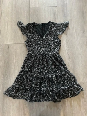 Volangklänning  - svart kortklänning med vita prickar och volangdetaljer. Klänningen har v-ringning, korta ärmar och knappar upptill. Tillverkad i ett lätt och luftigt material. 🖤 Jag är 165 cm. 🤍 endast använd 2 gånger  