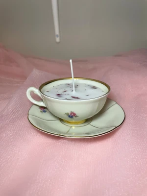 Doftljus med vaniljdoft i en tekopp med fat och blommig design  - Det här ljuset är gjort av återanvändbara material. Tekoppen är köpt secondhand och stearinet är från kyrkor som tänkte slänga det. Det här ljuset har en svag doft utav vanilj, så känsliga även kan använda det. Det här ljuset har även torkade blommor på som dekoration. 