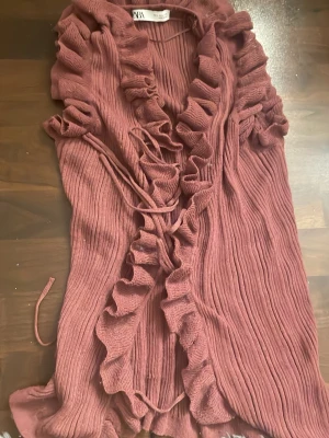  Zara -  ribbad kofta från Zara med volangkant längs hela öppningen och knytband i midjan. Koftan är ärmlös och har en mjuk, följsam struktur som ger en romantisk vibe. Perfekt för dig som gillar detaljer och vill ha något extra till din outfit.