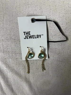 Guldörhängen med blå sten THE JEWELRY - Snygga örhängen från THE JEWELRY med droppformad blå sten infattad i guldfärgad metall. Örhängena har tunna kedjor som hänger ner för en trendig look. Perfekta för dig som vill sticka ut lite extra.