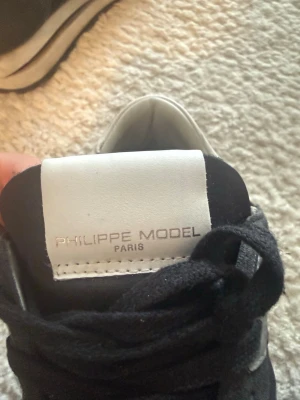 Philippe Model svarta sneakers - Stilrena svarta sneakers från Philippe Model Paris med vita detaljer. Skorna har en klassisk låg siluett, snörning och ovandel i en mix av mocka och mesh. Perfekta för dig som gillar en clean och modern look.