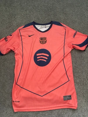 Barça matchtröja Raphinha 11 rosa Nike - Säljer en rosa FC Barcelona matchtröja från Nike med mörkblå detaljer och tryck. Tröjan har klubbmärke, Spotify-logga och nummer 11 med Raphinha på ryggen. Tillverkad i lätt, snabbtorkande material och har UNHCR-logga på baksidan.
