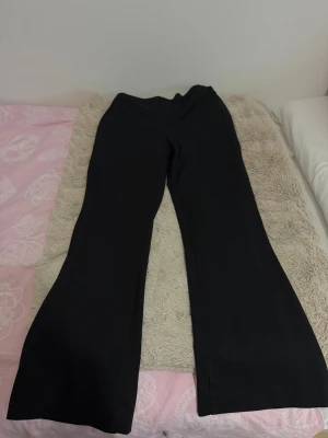 Svarta utsvängda kostymbyxor - Snygga svarta kostymbyxor med utsvängda ben och hög midja. Perfekta för en stilren look och passar till många olika outfits. Byxorna har en klassisk design utan synliga detaljer eller fickor framtill.