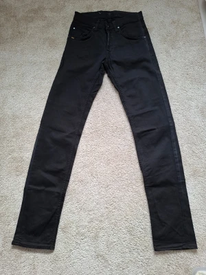 Svarta slim fit jeans - Säljer ett par svarta slim fit jeans med klassisk femficksdesign och normalhög midja. Jeansen har raka ben och är tillverkade i ett mjukt denimtyg med lite stretch för extra komfort. Tiger of sweden. 100 kr/st. Stl 28/34.