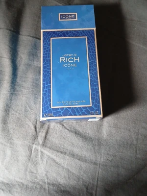 Johan B Rich Icône Eau de Toilette - Johan B Rich Icône Eau de Toilette för män, 90 ml. Flaskan är mörkblå med gulddetaljer och har en modern, fyrkantig form. Förpackningen är blå med guldramar och ett elegant mönster. En stilren parfym som ger en lyxig känsla.