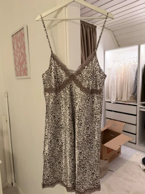 Två nattlinnen med spetsdetaljer - Säljer två nattlinnen i satin, ett med leopardmönster och bruna spetskanter, och ett vitt med svarta spetsdetaljer. Båda har smala axelband och v-ringning. Säljer båda ihop för 150