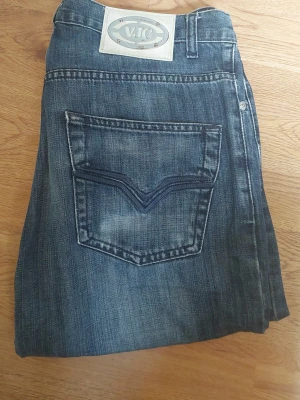 VJC - Säljer ett par blå jeans från VJC med raka ben och klassisk femficksdesign. Jeansen har en snygg tvättad look och en stor bakficka med V-formad söm. Perfekta för en avslappnad stil och tillverkade i slitstarkt denimtyg.