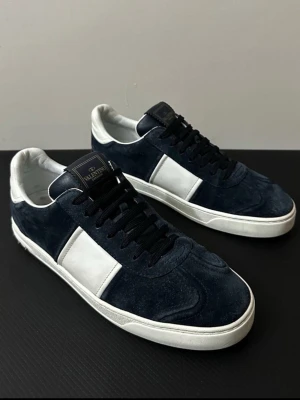 Valentino Flycrew  - Snygga sneakers från Valentino i mörkblå mocka med vita läderdetaljer och vit sula. Skorna har svarta skosnören och en klassisk låg siluett. Perfekta för dig som vill ha en stilren och exklusiv look med premiumkänsla.