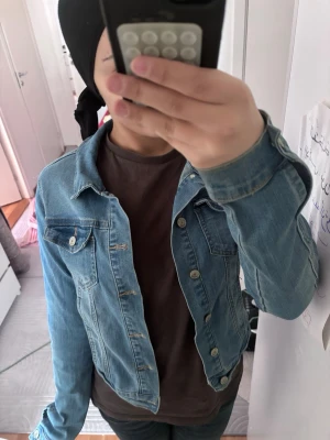  ljusblå jeansjacka - Snygg ljusblå jeansjacka med klassisk passform och silverfärgade knappar. Jackan har två bröstfickor med lock och knapp samt sömdetaljer framtill. Perfekt att slänga över en t-shirt för en avslappnad look.