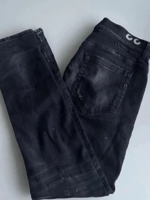 Dondup jeans  - Säljer ett par svarta jeans med coola slitningar och färgstänk för en trendig look. Jeansen har klassisk femficksmodell och rak passform. Perfekta för dig som gillar en avslappnad och edgy stil. Hör av er vid någon fundering! 
