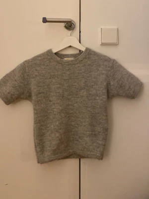 Grå stickad tröja Gina Tricot - Mysig grå stickad tröja från Gina Tricot. Tröjan har korta ärmar och rund hals med ribbad kant. Är i storlek 146-152 fast passar som en 134-140 efter som att jag har sytt om den. Skriv gärna om fler bilder🩷