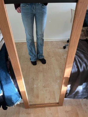 Ljusblå bootcut jeans - Säljer ett par ljusblå bootcut jeans med klassisk femficksmodell och normal midja. Jeansen har en avslappnad passform över låren och lätt utsvängda ben. Perfekta till sneakers eller boots för en casual look.