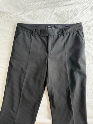 Svarta kostymbyxor från Filippa K - Snygga svarta kostymbyxor från Filippa K med diskreta kritstrecksränder. Byxorna har raka ben, pressveck, hällor för bälte och fickor både fram och bak. Materialet är troligtvis en ullblandning som ger en klassisk och stilren look. Nypris 1500-2500kr