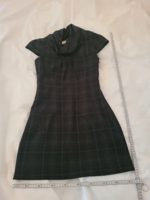 Mörkgrå rutig klänning med krage - Snygg mörkgrå kortklänning med diskret rutigt mönster och bred krage. Klänningen har korta ärmar och lätt utställd passform. Perfekt för dig som gillar en stilren look med lite edge.