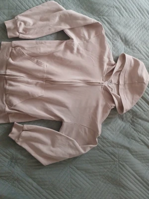 Ljusbeige hoodie med dragkedja H&M - Ljusbeige hoodie från H&M med dragkedja framtill och två fickor. Klassisk modell med huva och ribbade muddar vid ärmslut och nederkant. Perfekt för en chill och avslappnad stil.