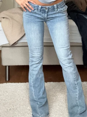 Ljusblå bootcut jeans True Religion - Säljer ett par ljusblå bootcut jeans från True Religion med klassiska kontrastsömmar och dekorativa ficklock bak. Jeansen har låg midja och är tillverkade i denim med stretch för skön passform. Perfekta för dig som gillar snygga detaljer.