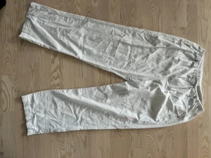 Vita linnebyxor med resårmidja - Säljer ett par vita linnebyxor med avslappnad passform och resår i midjan. Byxorna har sidofickor och små röda sömdetaljer vid fickorna. Perfekta för en chill och stilren look.