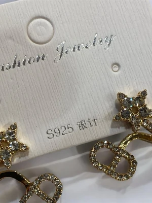 Guldiga stjärnörhängen med strass - Snygga örhängen i guldton med stjärnformade detaljer och glittrande strass. Örhängena är tillverkade i S925 silver och har även dekorativa former undertill, täckta av små stenar för extra bling.
