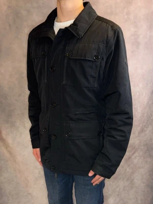 Svart J-Lindeberg Fieldjacket - Stl M - Riktigt snygg Vår/Höst Fieldjacket från J-Lindeberg i färgen svart! | Mycket bra skick: 9/10, inga defekter, mindre användningspår | Stl: M, modellen är 177cm och väger 75kg, passar bättre om du är längre 🙌  | Hör av dig vid frågor // Galgen 🫡