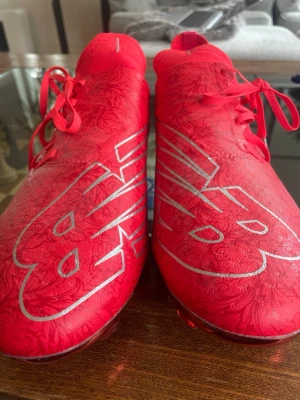 Röda New Balance fotbollsskor ( kvitto från unisport finns) - Snygga röda fotbollsskor från New Balance med stora vita NB-loggor på ovansidan och diskret mönster i materialet. Har använts i endast 15 minuter. Helt autentiskt köpt för 2 års sen. 