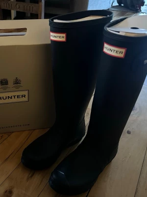 Svarta höga gummistövlar från Hunter - Säljer ett par klassiska svarta höga gummistövlar från Hunter. Knäppe på sidan. Helt nya. 