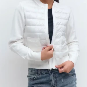 Vit quiltad cardigan jacka - Snygg vit cardigan jacka med quiltad framsida och två fickor. Jackan har dragkedja och ribbade muddar vid ärmslut och nederkant. Perfekt för dig som gillar stilren och enkel design med en modern touch.