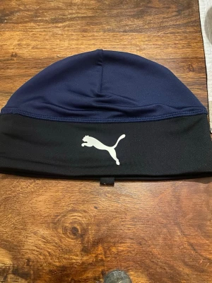 Mörkblå och svart mössa från Puma - Snygg mössa från Puma i mörkblått och svart med den klassiska vita Puma-loggan framtill. Tillverkad i ett stretchigt och mjukt material som sitter skönt på huvudet. Perfekt för kalla dagar och sportiga outfits. Kolla gärna mina andra annonser❗️