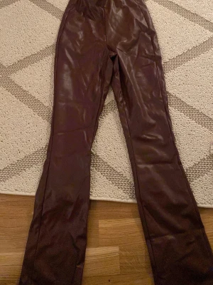 Bruna PU-byxor från Kappahl - Snygga bruna byxor i fuskläder (PU) från Kappahl. Byxorna har raka ben och resår i midjan för en bekväm passform. Perfekta för dig som vill ha en trendig look med skinnkänsla. Det är 2 byxor samma storlek 