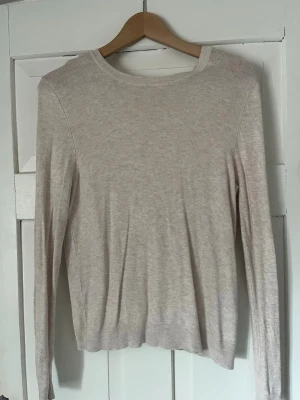 Beige stickad tröja Basic You - Ljusbeige stickad tröja från Basic You med rund halsringning och långa ärmar. Tröjan har en enkel och stilren design i tunt, mjukt material som passar perfekt till lager på lager. Ribbstickade muddar vid ärmslut och nederkant.