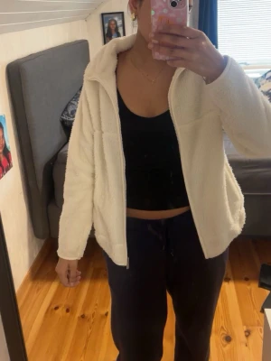 Vit fleece med dragkedja - Mysig vit fleece  med dragkedja framtill och hög krage. Jackan har en avslappnad passform och är gjord i fluffigt, mjukt material som ger en skön och trendig look. Perfekt för att hålla värmen under kyliga dagar.
