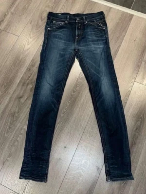 Mörkblå skinny jeans från Nudie - Säljer ett par mörkblå skinny jeans från Nudie med snygga slitningar och klassiska fem fickor. Jeansen har orangea sömmar och en patch bak i midjan. Perfekta för dig som gillar en smal passform och tidlös stil.
