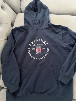 Hoodie Vinson polo club  - Mörkblå hoodie från Vinson med tryck i vitt och rött framtill där det står 'Original Legendary Traditions'. Hoodien har stor huva och magficka samt ribbade muddar vid ärmar och nederkant. Perfekt för en avslappnad och sportig stil.