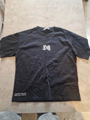 Svart t-shirt med tryck - Svart t-shirt med vitt tryck på bröstet Klassisk passform och rund halsringning. Perfekt för en avslappnad stil.