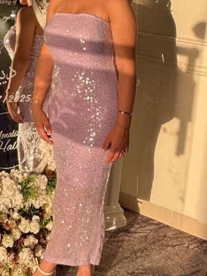 Axelbandslös långklänning från GINATRICOT - Axelbandslös långklänning i ljuslila med glittriga paljetter. Klänningen har en figurnära passform och är tillverkad i ett stretchigt material som ger en elegant siluett. Perfekt för speciella tillfällen när du vill sticka ut. Storlek M , men passar även för mig som är storlek S . Köpt för 800kr kan diskutera pris har använt den 1 gång