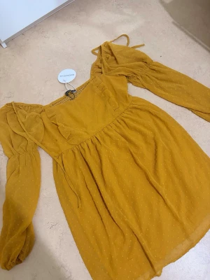 Gul prickig klänning från bohoo  - Söt gul kortklänning från bohoo med diskret prickigt mönster. Klänningen har långa puffärmar, volangdetaljer framtill och knytband vid axlarna. 