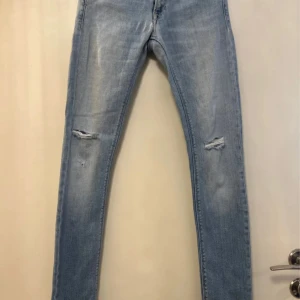 Ljusblå jeans med slitningar Replay - Snygga ljusblå jeans med slitningar på knäna från Replay. De har en tight passform och är perfekta för en avslappnad stil. Klassisk femficksdesign och dragkedja.