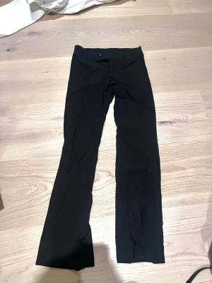 Svarta lågmidjade kostym byxor - Svarta lågmidjade kostymbyxor med utsvängda ben. Byxorna har två knappar framtill och är sydda i ett stretchigt tyg som ger en snygg passform. Perfekta för dig som gillar en stilren och enkel look.