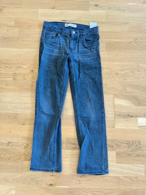 Blå raka jeans från Levi's - Klassiska blå jeans från Levi's med rak passform och fem fickor. Jeansen har en enkel design med synliga sömmar och Levi's ikoniska röda etikett på bakfickan. Perfekta för en avslappnad och tidlös stil.