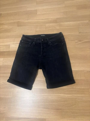 Svarta jeansshorts med uppvik - Snygga svarta jeansshorts från Jack & Jones med klassisk femficksdesign och uppvikta benslut. Shortsen har normal passform och är tillverkade i bomull med en liten mängd stretch för extra komfort. Perfekta för en avslappnad stil under varma dagar.